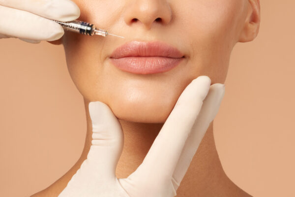 Lip injections concept. Young lady getting beauty injection in her lips, beautician holding syringe with filler next to woman mouth, cropped